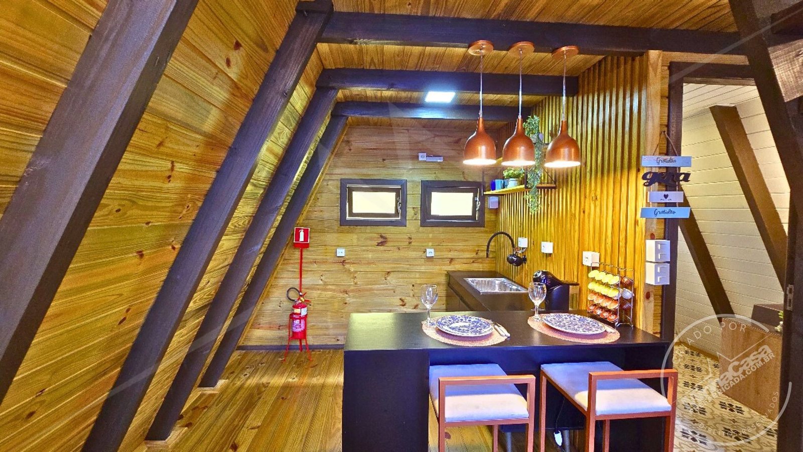 Mesa de Cozinha com Vista do Banheiro – A‑Frame 1 (51,77 m²) Vista da mesa da cozinha em direção ao banheiro, no chalé A‑Frame 1 com pinus tratado