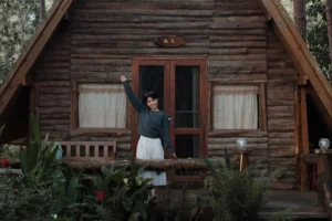Mulher sorrindo enquanto acena na frente de um chalé de madeira, ilustrando como fazer casa de madeira.